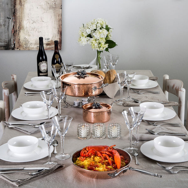 Table set for family meal complete with copper cookware set, seafood pasta, and wine.