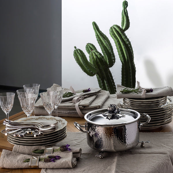 Soup pot on a table with plates, glasses, silverware, and a couple cacti.